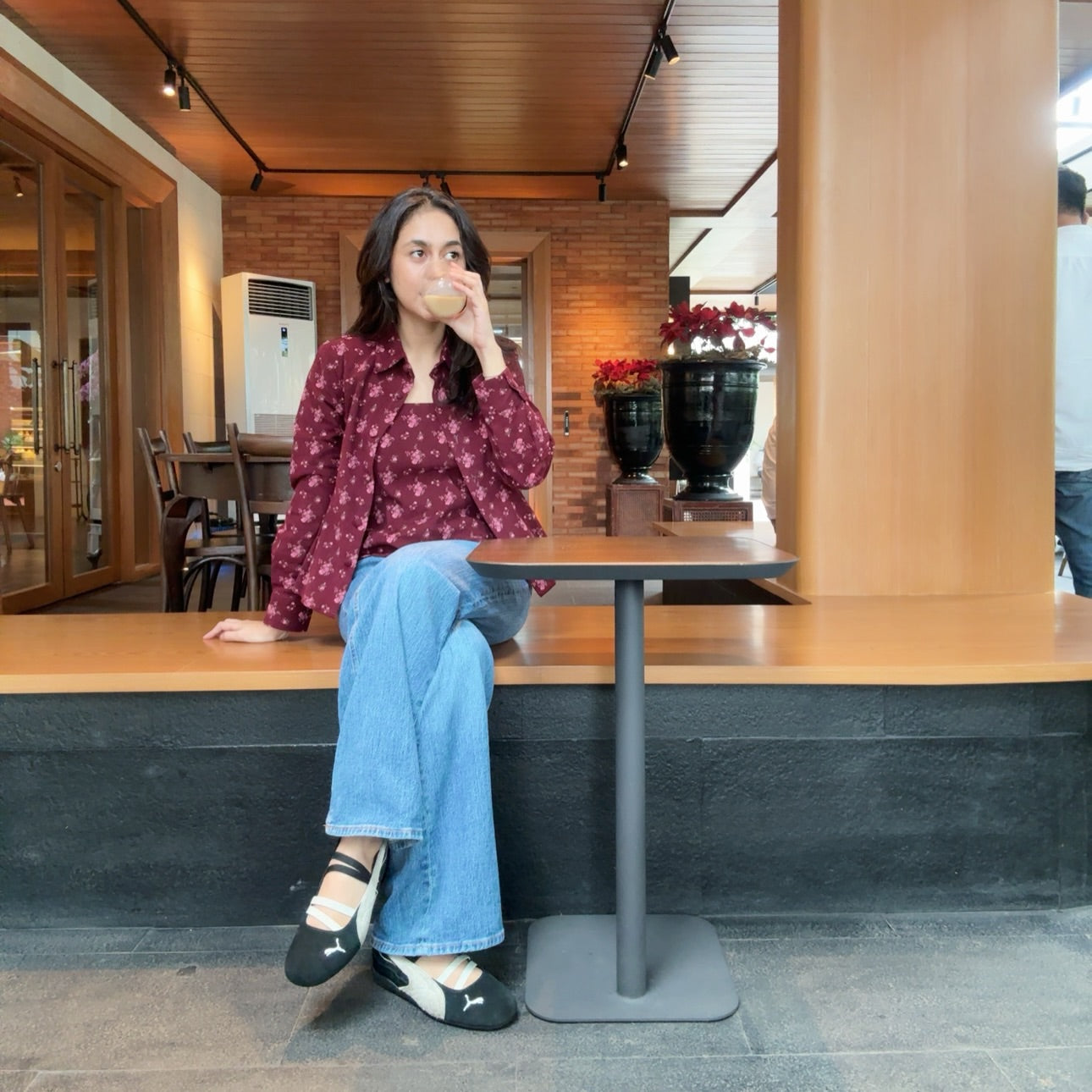 Woman sitting at a cafe counter drinking from a cup wearing dolly burgundy